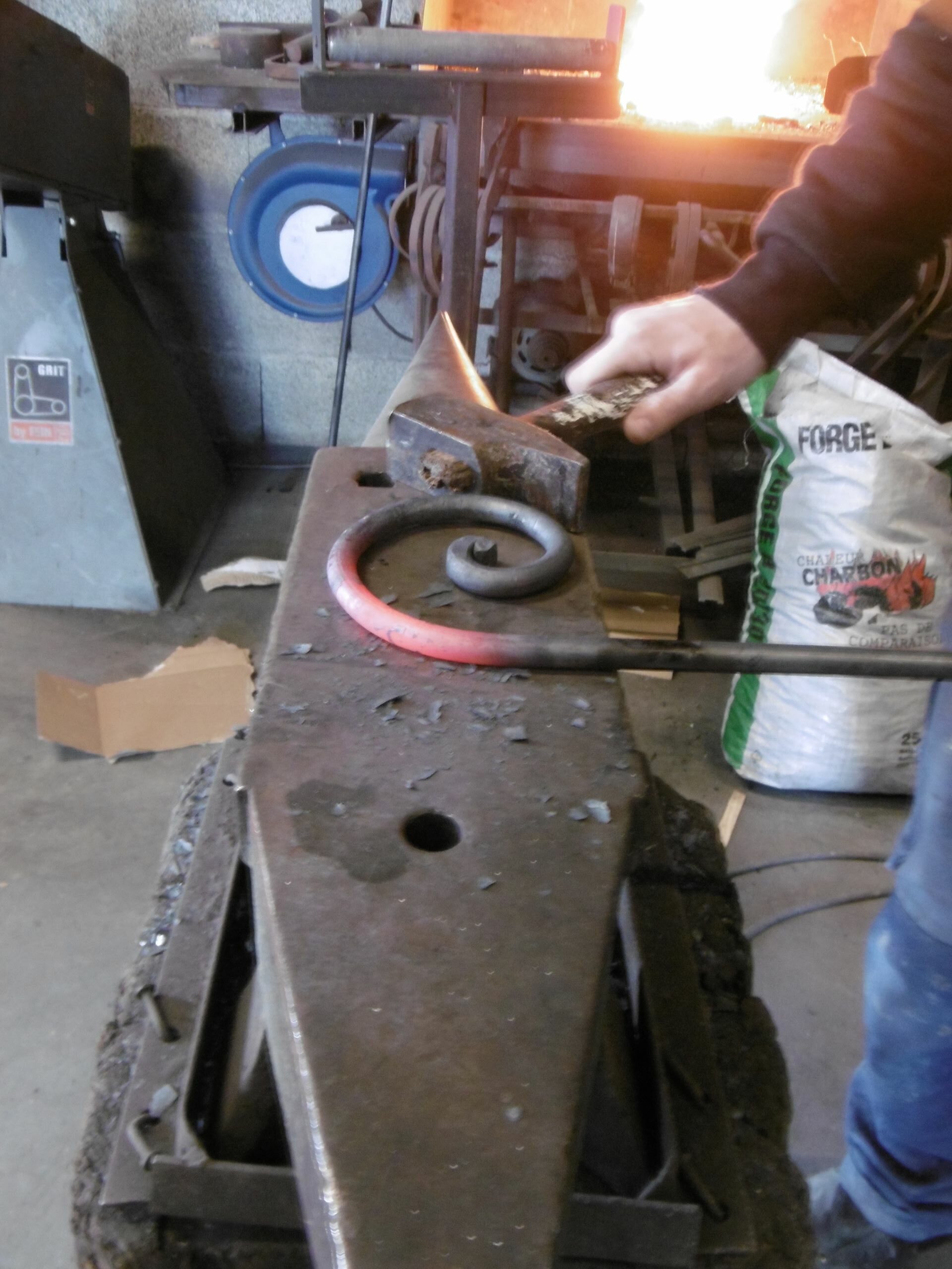main forgeant une volute métallerie des amandiers